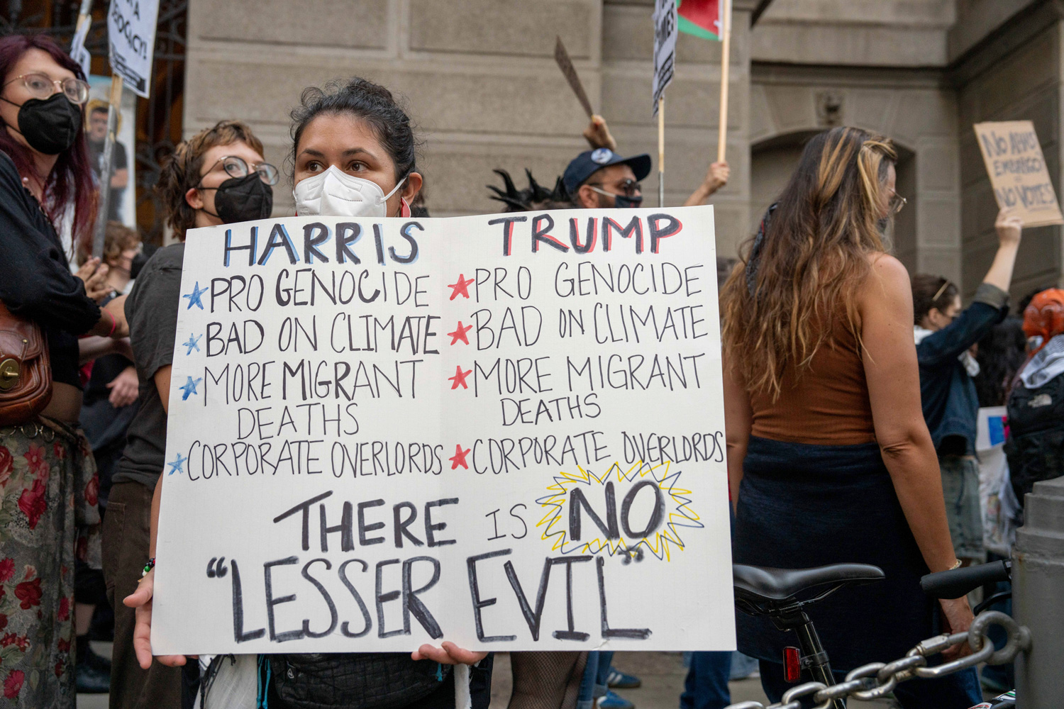 Protestors on a sidewalk hold a sign that reads There is NO Lesser Evil